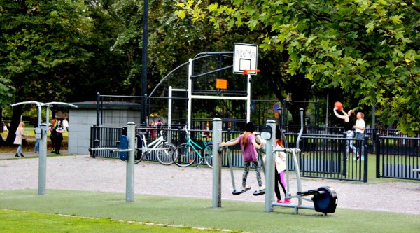  Kuvassa etualalla aikuisten kuntoiluvälineet ja taustalla pelialue. Leikkialueita puistossa on kolme. 