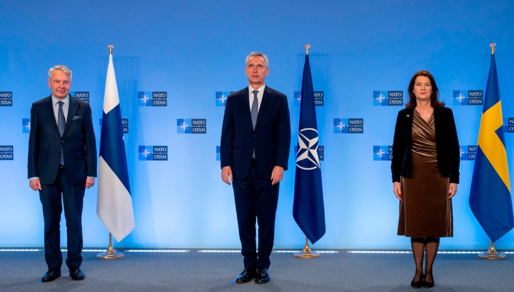 Ministerit seisovat maidensa lippujen edessä, heidän välissään pääsihteri takanaan Naton lippu.