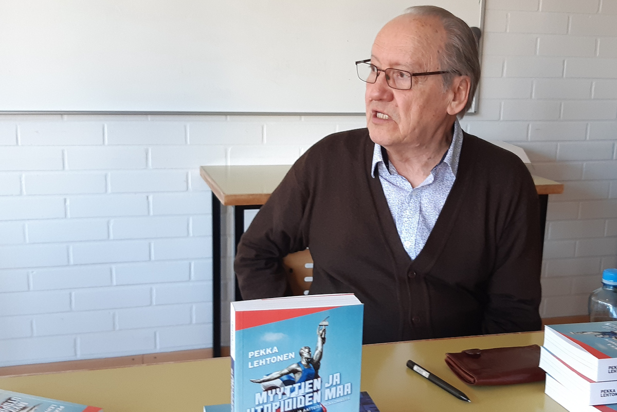 Pekka Lehtonen istuu pöydän ääressä. Pöydällä on hänen kirjansa "Myyttien ja utopioiden maa".