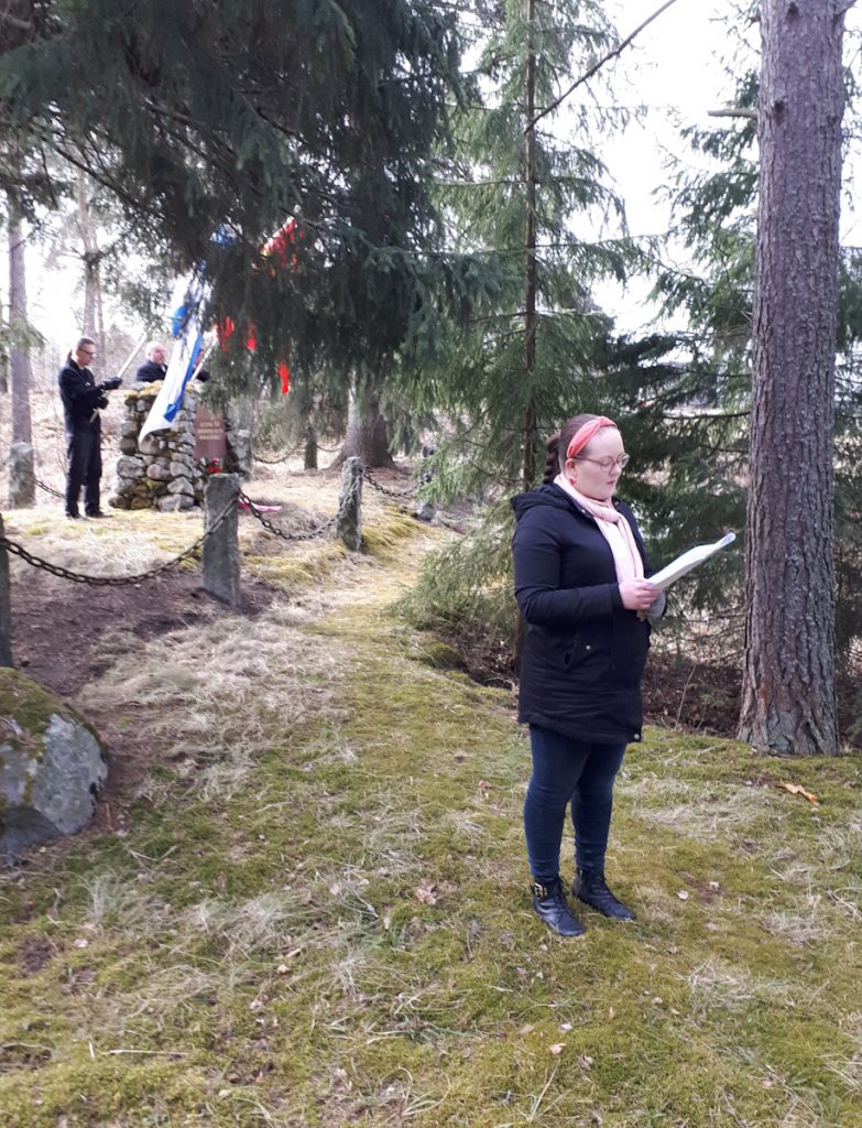 Mira Nurmi puhumassa taustalla metsää ja hautamuistomerkki