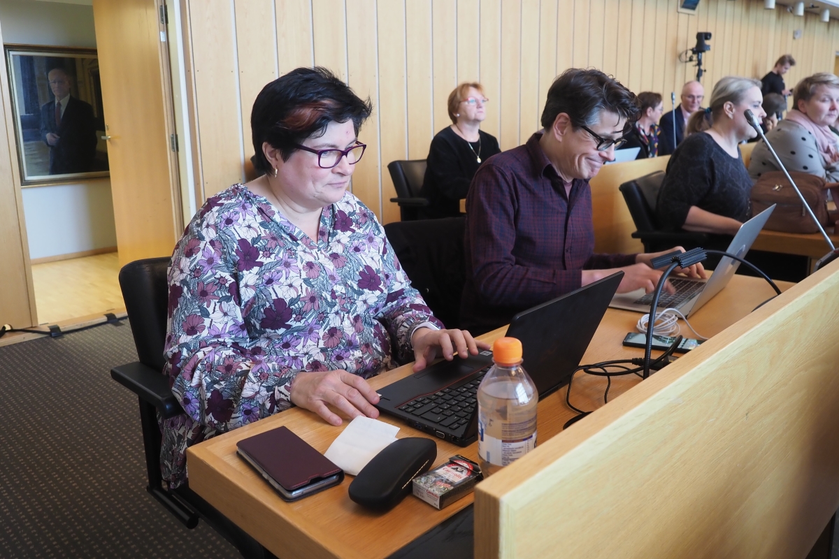 Leena Saarela ja Jouni Sirén istumassa valtuustosalissa vierekkäin tietokoneiden äärellä.