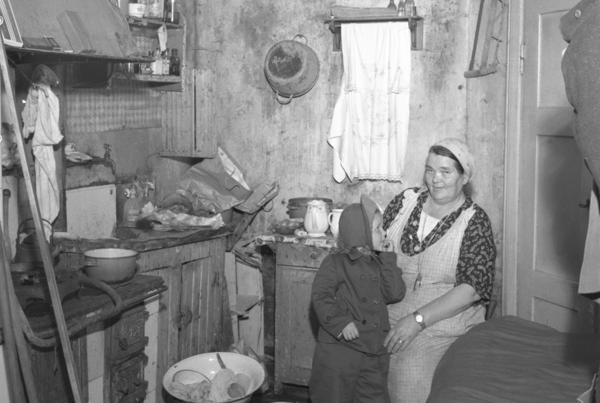 Mustavalkoinen kuva keittiöstä, jossa nainen ja lapsi.